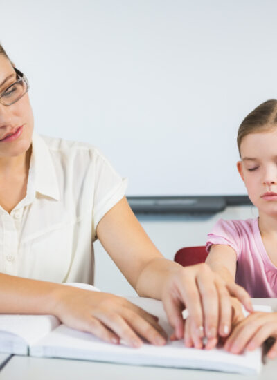 Teacher,Assisting,Blind,Student,In,Library,At,School